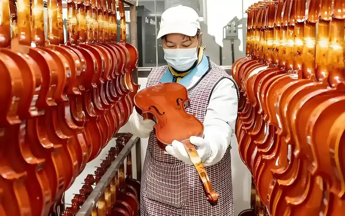 Violin factory worker inspecting handcrafted violins in workshop for wholesale production