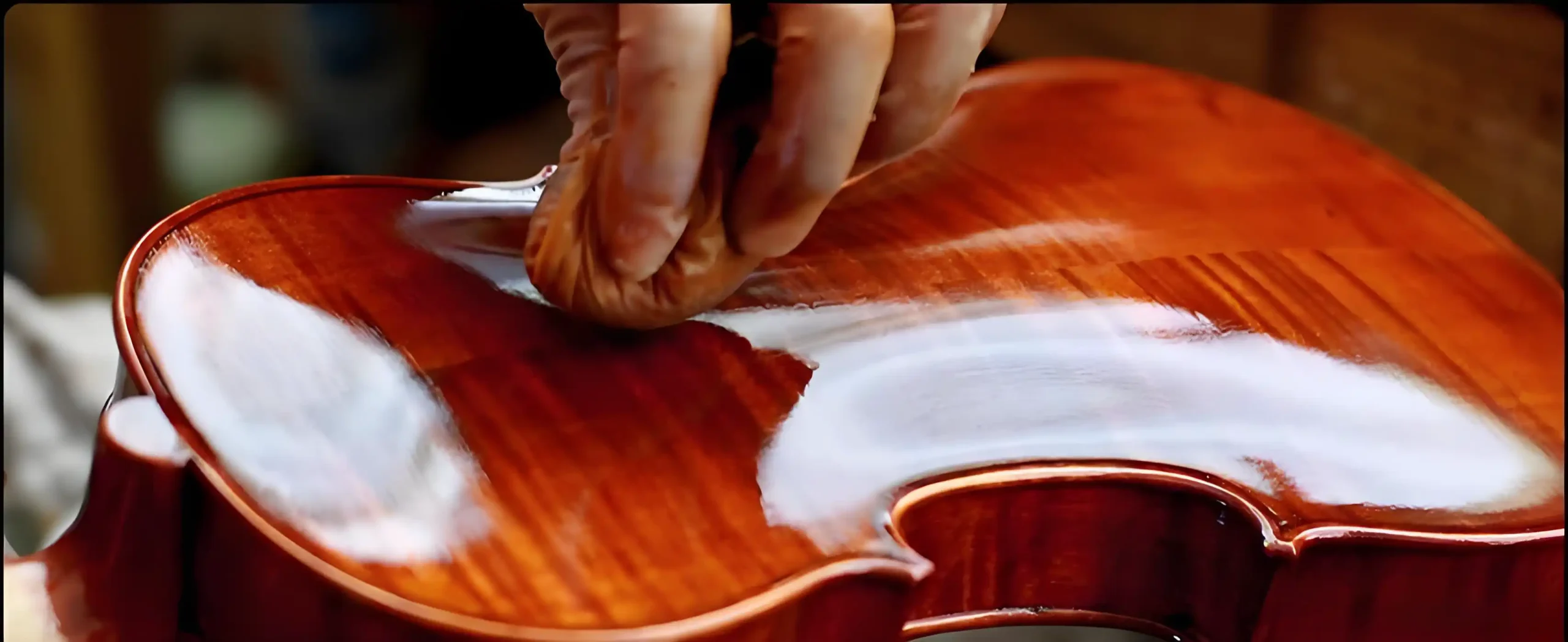 A photo of a luthier polishing a violin in a focused, solitary moment.