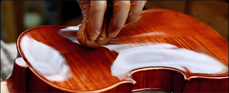 A luthier polishing a violin in a focused, solitary moment.